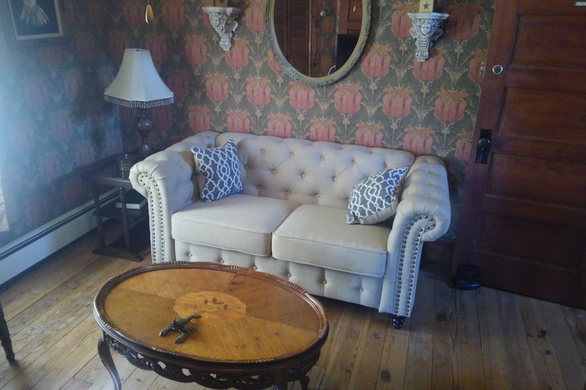 A room with a tufted sofa, a round wooden coffee table, and a mirror on the wall.
