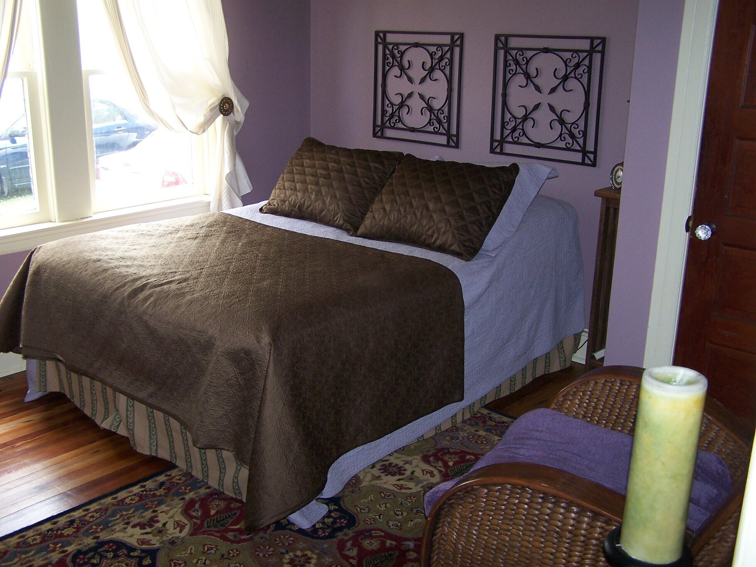 Une chambre à coucher avec un lit, une fenêtre avec des rideaux, un tapis à motifs et deux éléments de décoration murale.