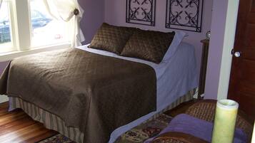 Une chambre à coucher avec un lit, une fenêtre avec des rideaux, un tapis à motifs et deux éléments de décoration murale.
