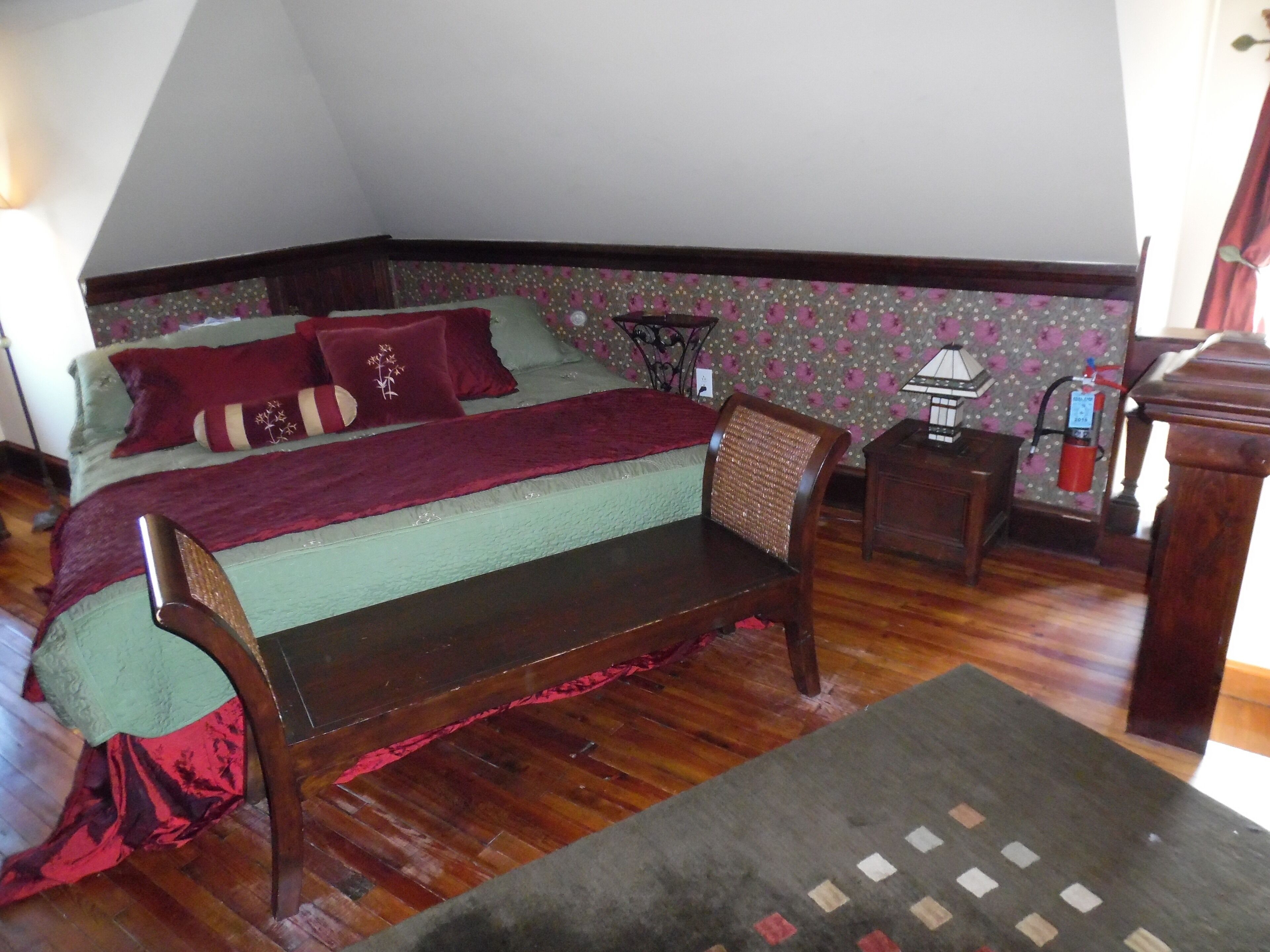 A bedroom with a bed, a wooden chair, a nightstand, and a lamp.