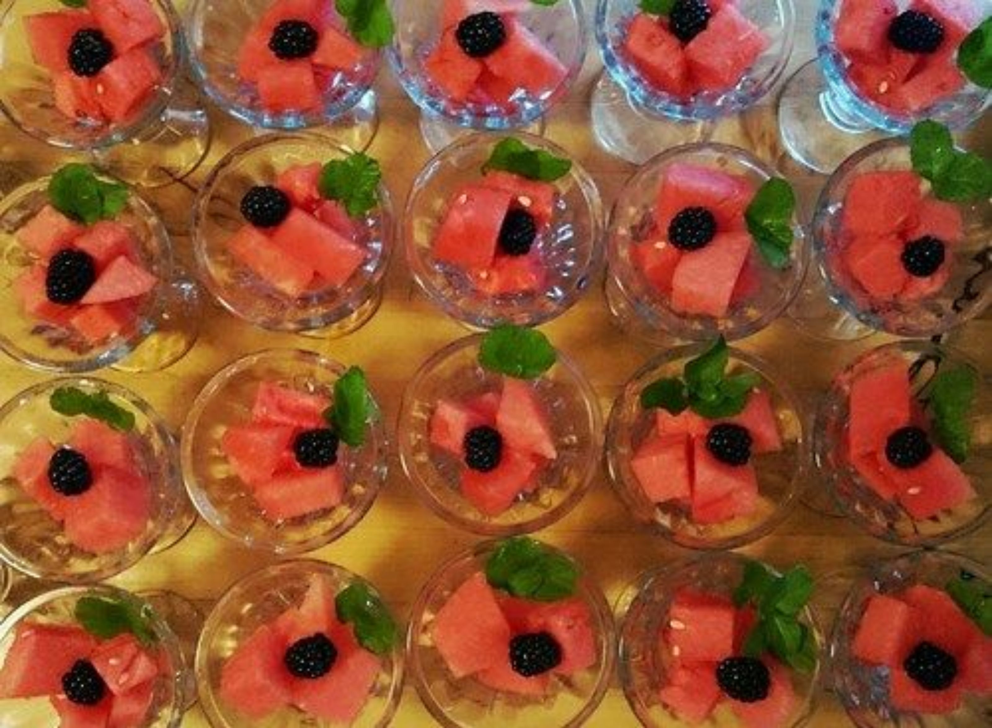 A tray of small glasses filled with watermelon slices and blackberries, garnished with mint leaves.