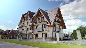 A multi-story residential building with a stone facade, multiple balconies, and a gated driveway. - Pod Hawraniem (Bukowina Tatrzanska)