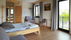 A bedroom with a wooden bed, a grey sofa, a chair, a wardrobe, a window with curtains, and a balcony with a railing. - Pod Hawraniem (Bukowina Tatrzanska)