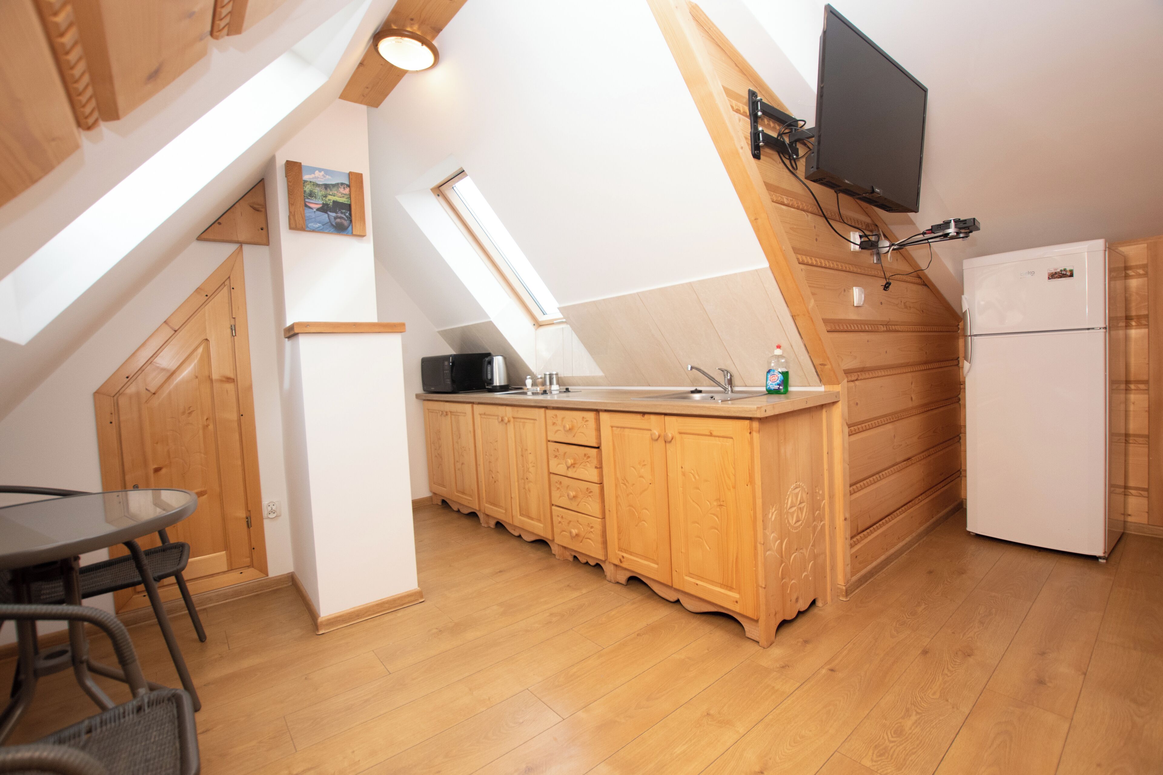 Une cuisine avec des meubles de rangement en bois, un four encastré et un téléviseur fixé au mur.