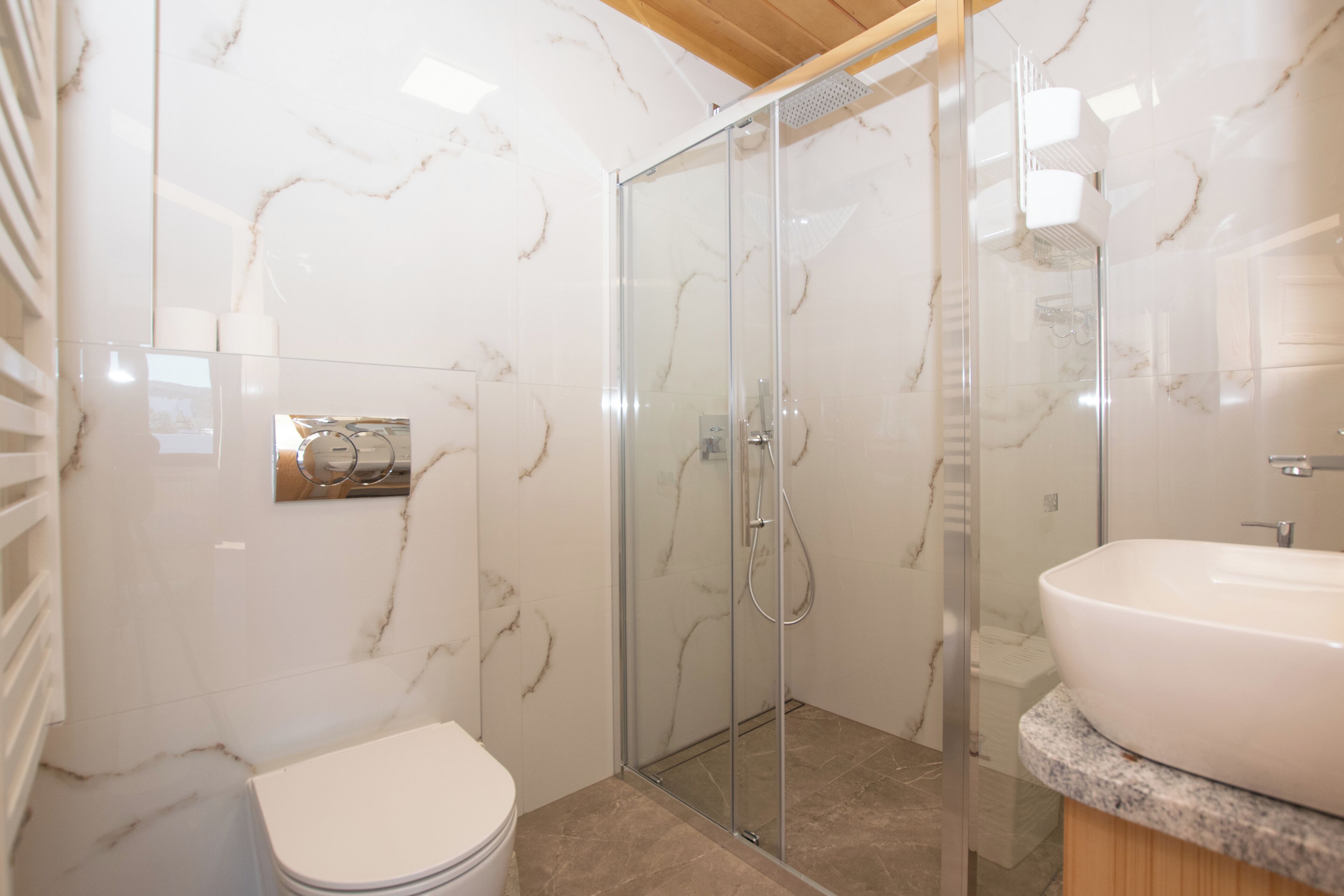 Un baño moderno con cabina de ducha de vidrio, un lavabo blanco y un revestimiento de mármol en la pared.