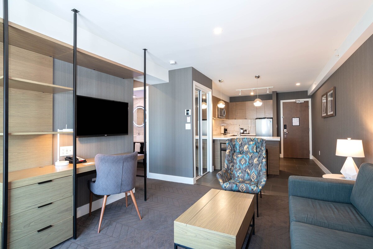 A modern living room with a flat-screen TV, a desk, a chair, a sofa, and a coffee table.