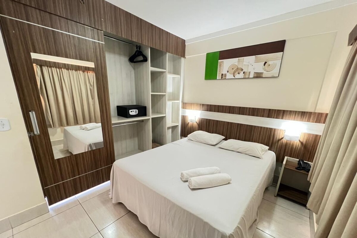 A hotel room with a bed, a bedside table, a mirror, a wardrobe, and a wall-mounted artwork.