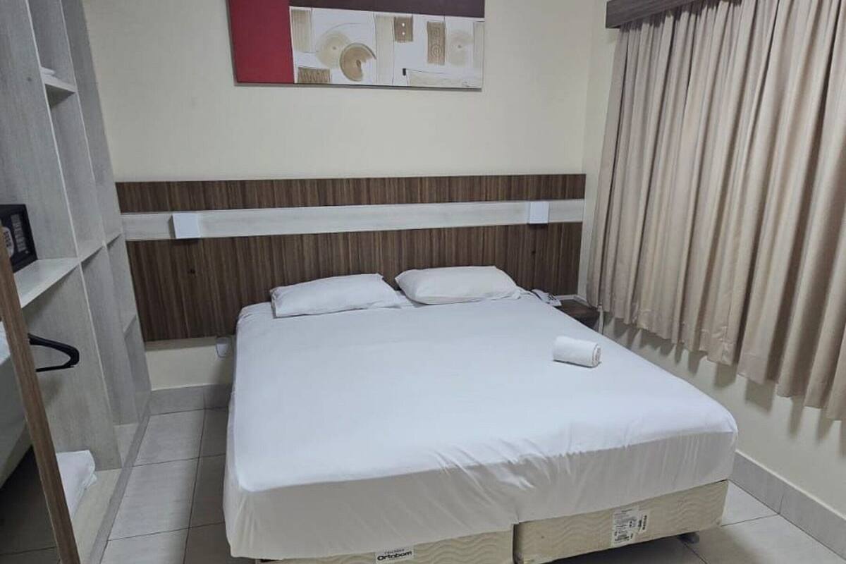 Ein Hotelzimmer mit Bett, Schrank, Spiegel und einem Fenster mit Vorhängen.
