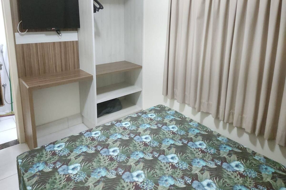 Ein Schlafzimmer mit einem Bett, einem an der Wand befestigten Fernseher, einem Kleiderschrank und einem Fenster mit Vorhängen.