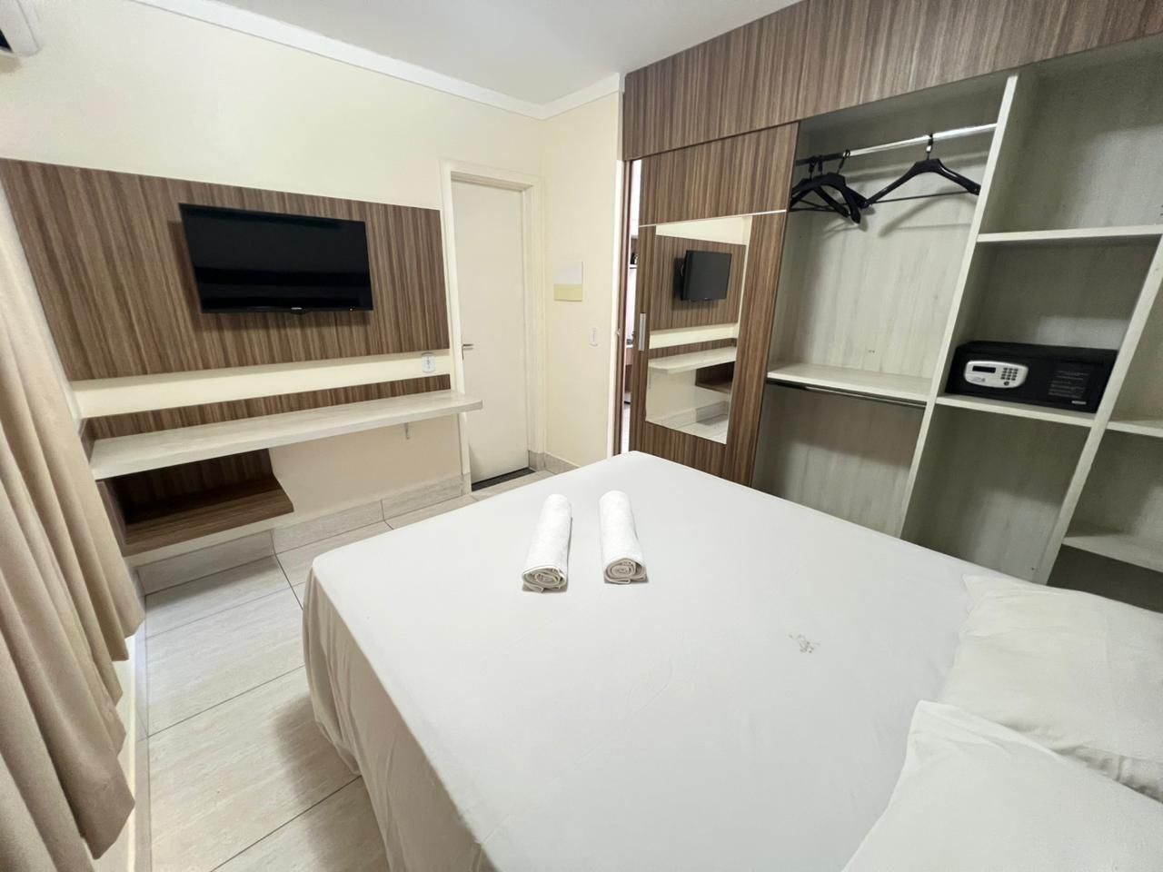 Habitación de hotel con cama, televisor montado en la pared, armario y estante con microondas.