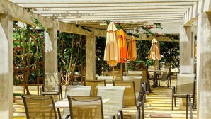 A covered outdoor seating area with tables and chairs, umbrellas, and a pergola structure. - Apartment Lacqua DiRoma IV - JC Temporada (Caldas Novas)