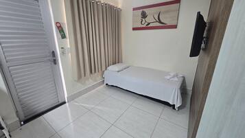 Quarto com cama, cortina, TV fixada na parede e porta.