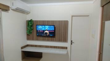 A room with a mounted TV, wooden shelves, a door, and a small plant.