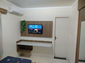 Una habitación con una televisión montada, estanterías de madera, una puerta y una pequeña planta.