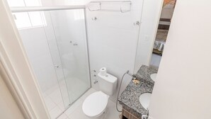 A bathroom with a glass shower enclosure, a toilet, a sink with a granite countertop, and a towel rack. - Apartment Lacqua DiRoma IV - JC Temporada (Caldas Novas)