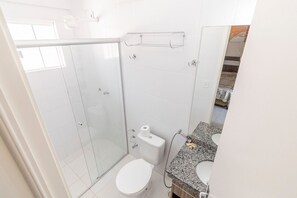 Et badeværelse med brusekabine i glas, toilet, vask med granitbordplade og et håndklædestativ.