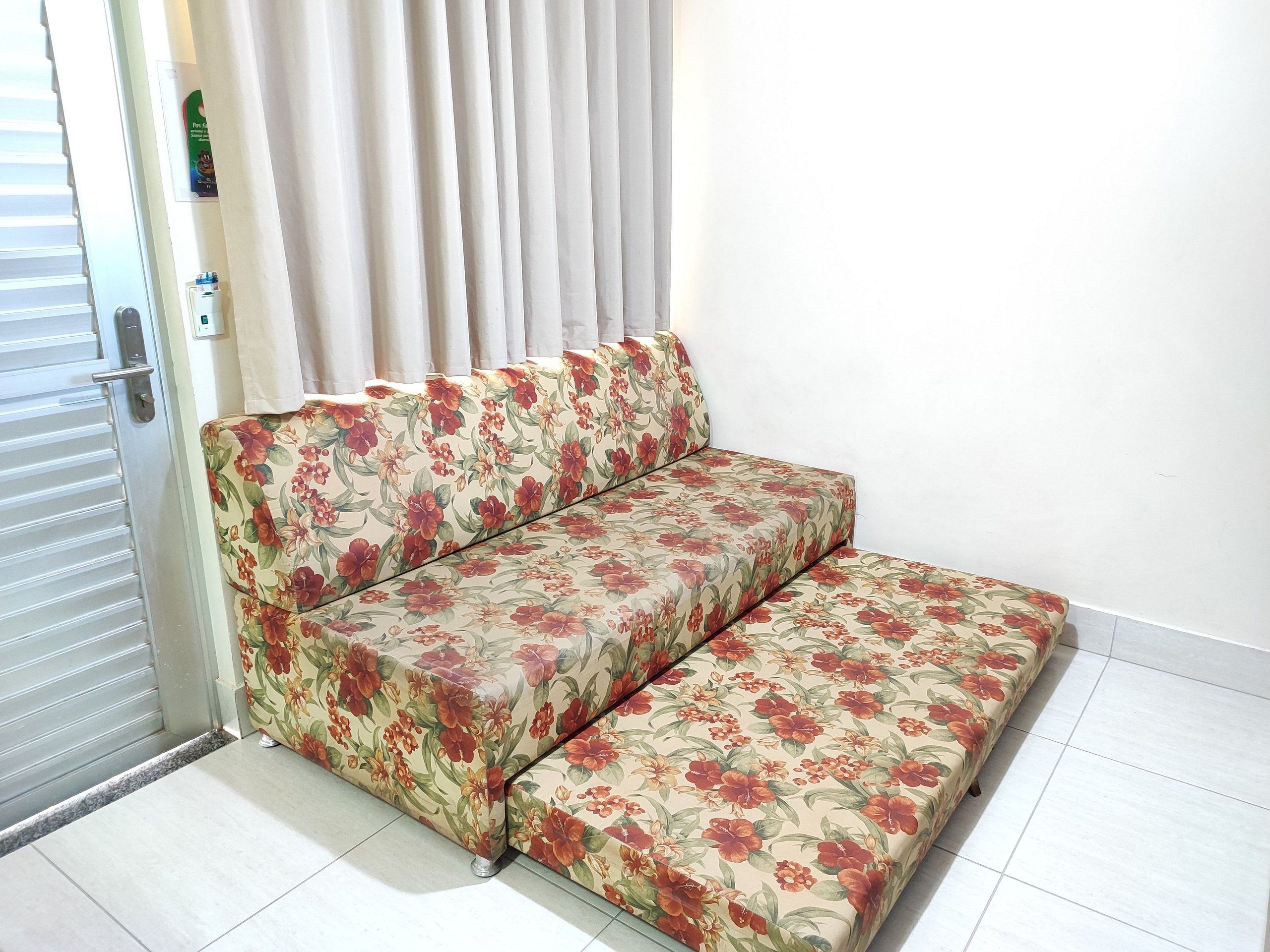 Ein Sofa mit floralem Bezug in einem Raum mit Fliesenboden und geschlossener Tür.