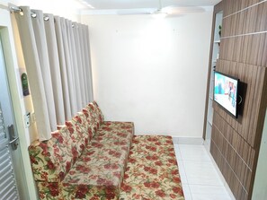 Ein Zimmer mit einer Couch, einem an der Wand montierten Fernseher und einem Vorhang.