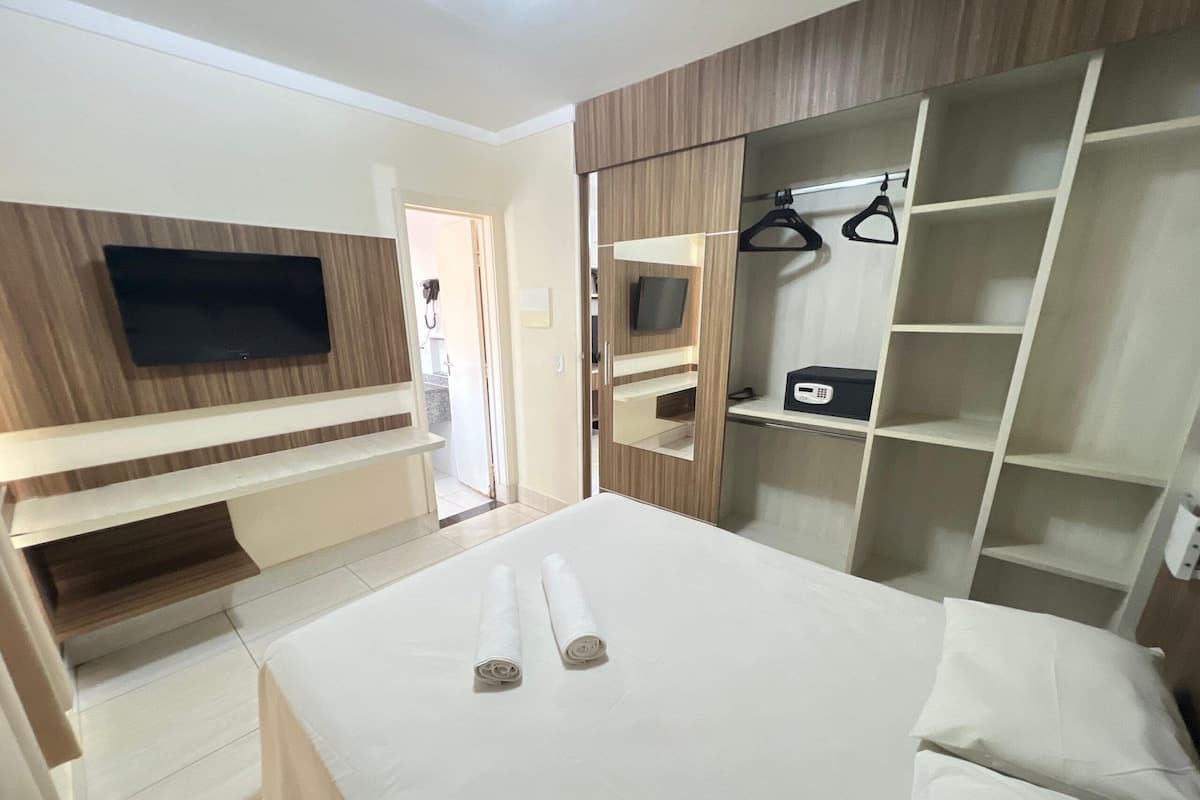 Ein modernes Hotelzimmer mit Bett, einem an der Wand befestigten Fernseher, einem Kleiderschrank mit Kleiderstange und einem Schreibtisch.