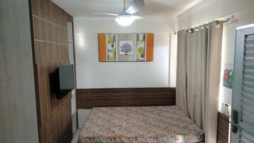 A bedroom with a bed, a ceiling fan, a wall-mounted TV, and a door with a curtain.