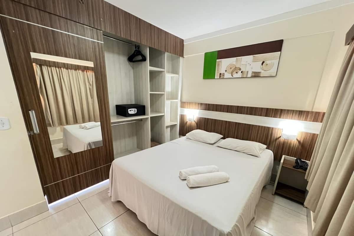 Ein Hotelzimmer mit Bett, Nachttisch, Spiegel, Kleiderschrank und einem Wandbild.