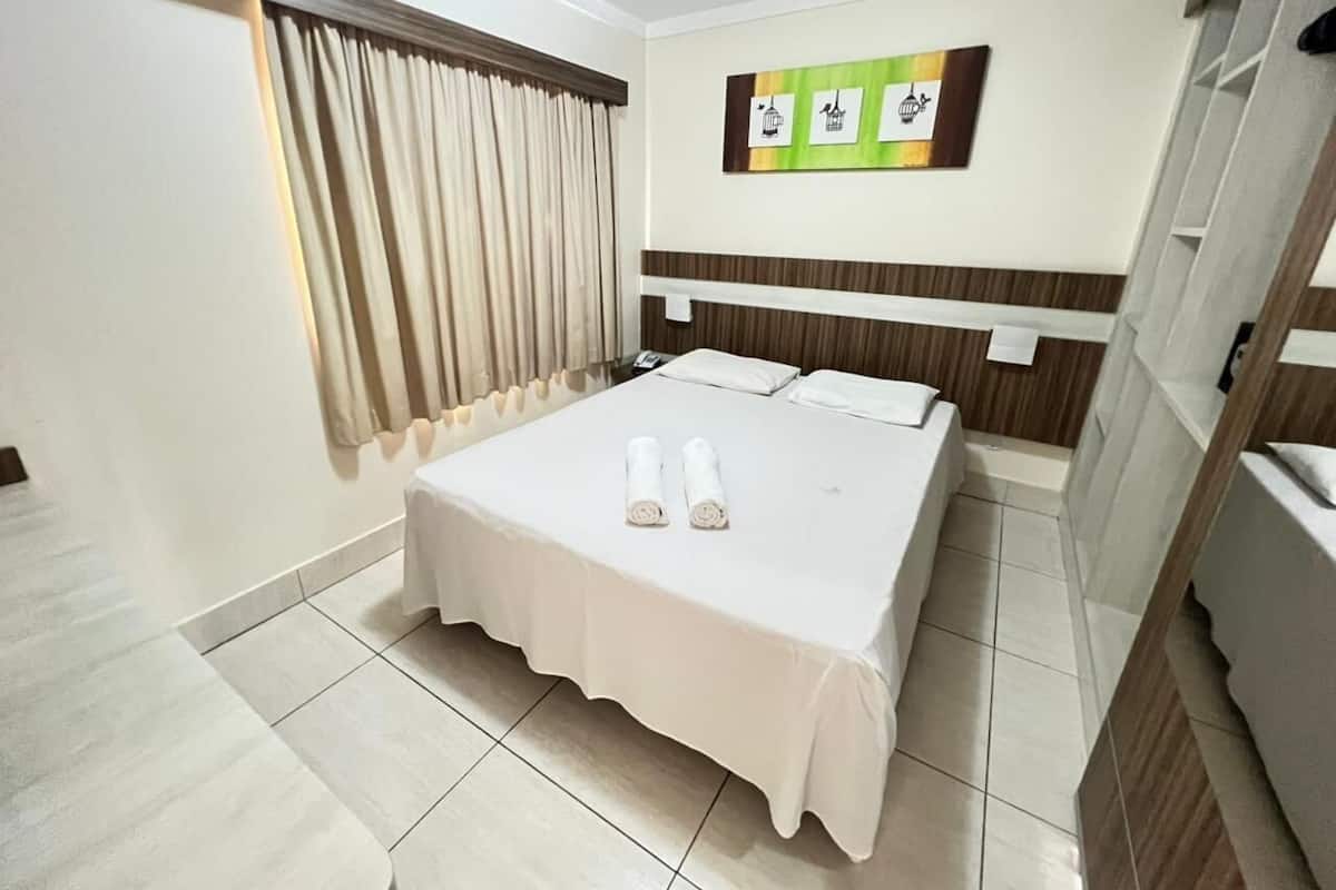 Ein Hotelzimmer mit Bett, einem Vorhangfenster, einem Wandbild und einem Fliesenboden.