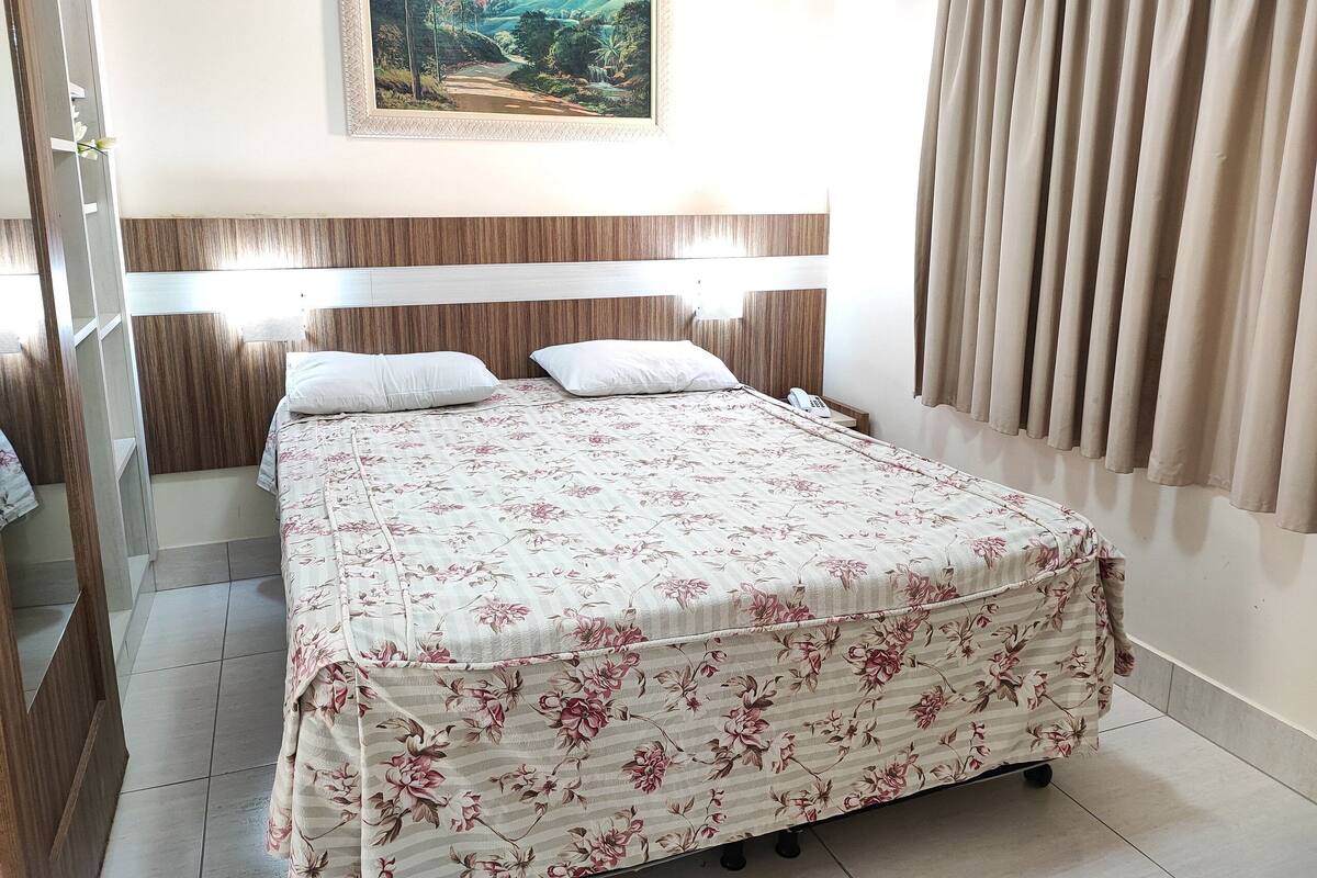 Ein Hotelzimmer mit einem Bett, einem Bild an der Wand, einem Telefon und Vorhängen.