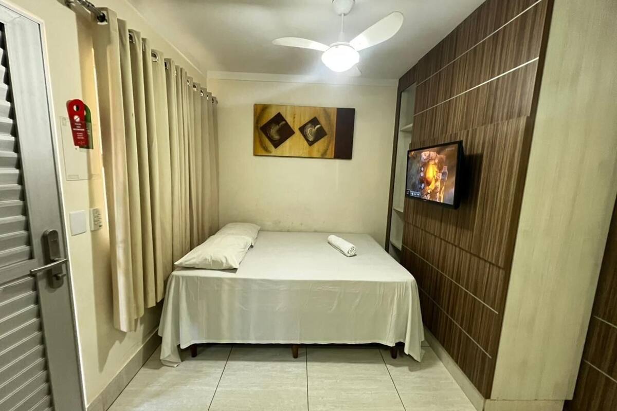 Ein Hotelzimmer mit Bett, Vorhängen, Deckenventilator, Flachbildfernseher und einer Wandpaneele aus Holz.