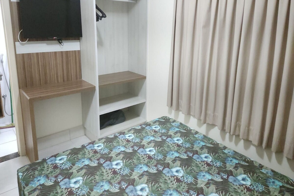 A bedroom with a bed, a TV mounted on a wall, a wardrobe, and a window with curtains.