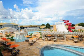 A resort with a swimming pool, lounge chairs, umbrellas, and a red slide.