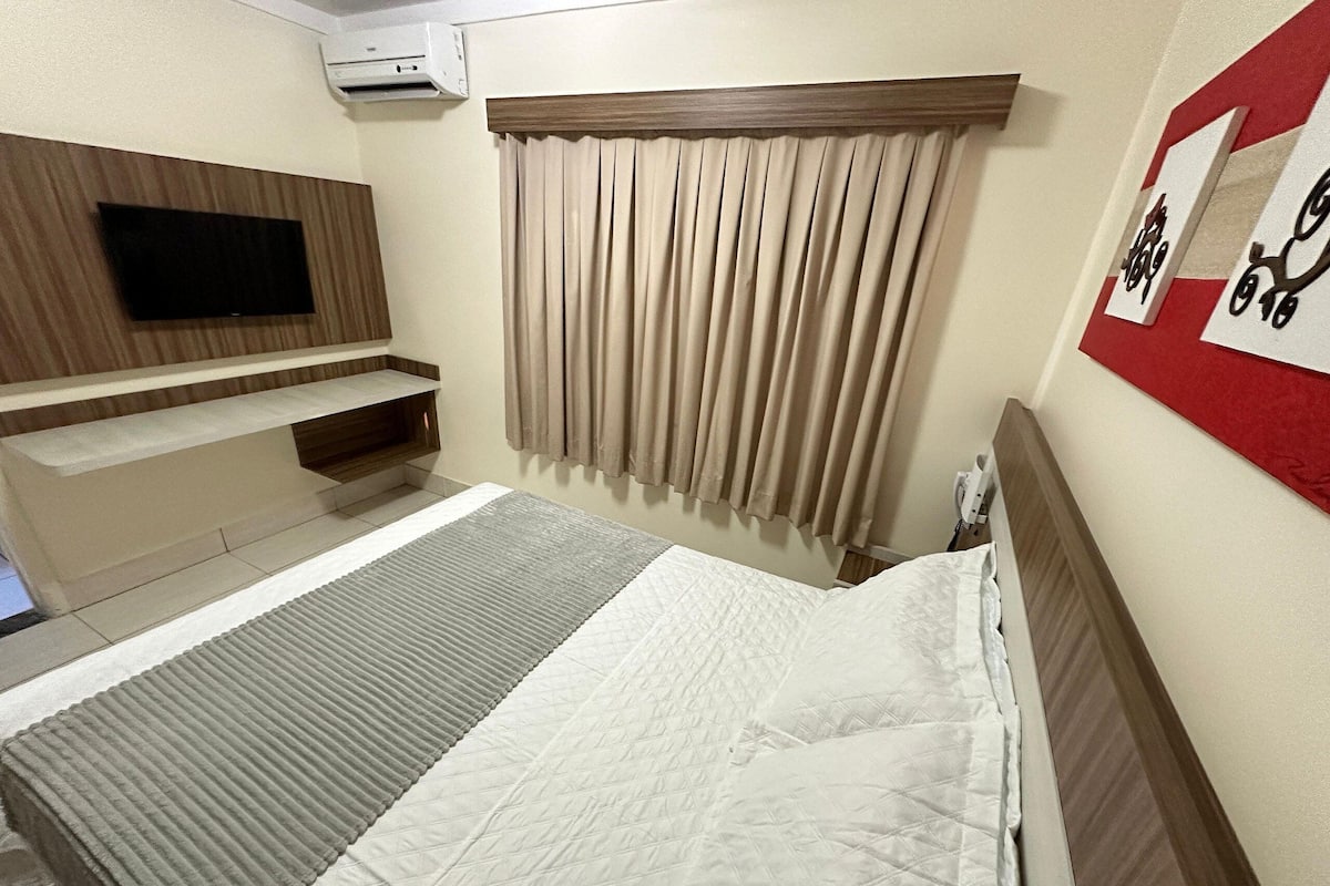 Ein Hotelzimmer mit Bett, Flachbildfernseher an der Wand, einem Fenster mit Vorhängen und einer Wandklimaanlage.