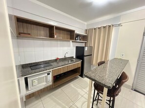 A compact kitchen with a built-in microwave, a sink, and a refrigerator. - Apartment Lacqua DiRoma IV - JC Temporada (Caldas Novas)