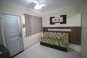 A room with a closed door, a ceiling fan, a sofa with a floral pattern, a wall-mounted picture frame, and a tiled floor. - Apartment Lacqua DiRoma IV - JC Temporada (Caldas Novas)