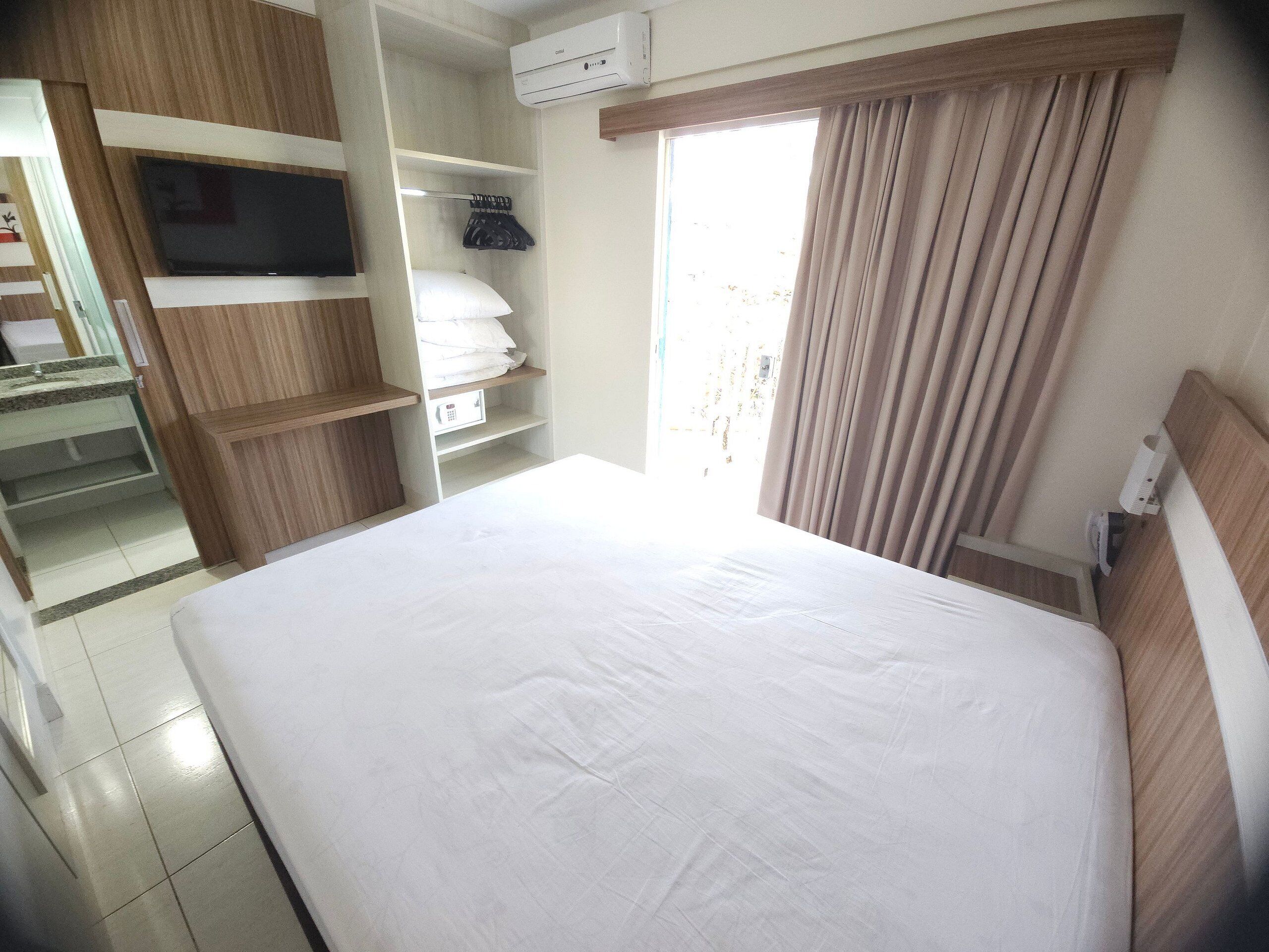Une chambre d’hôtel avec un lit, une télévision, une armoire et une fenêtre avec des rideaux.