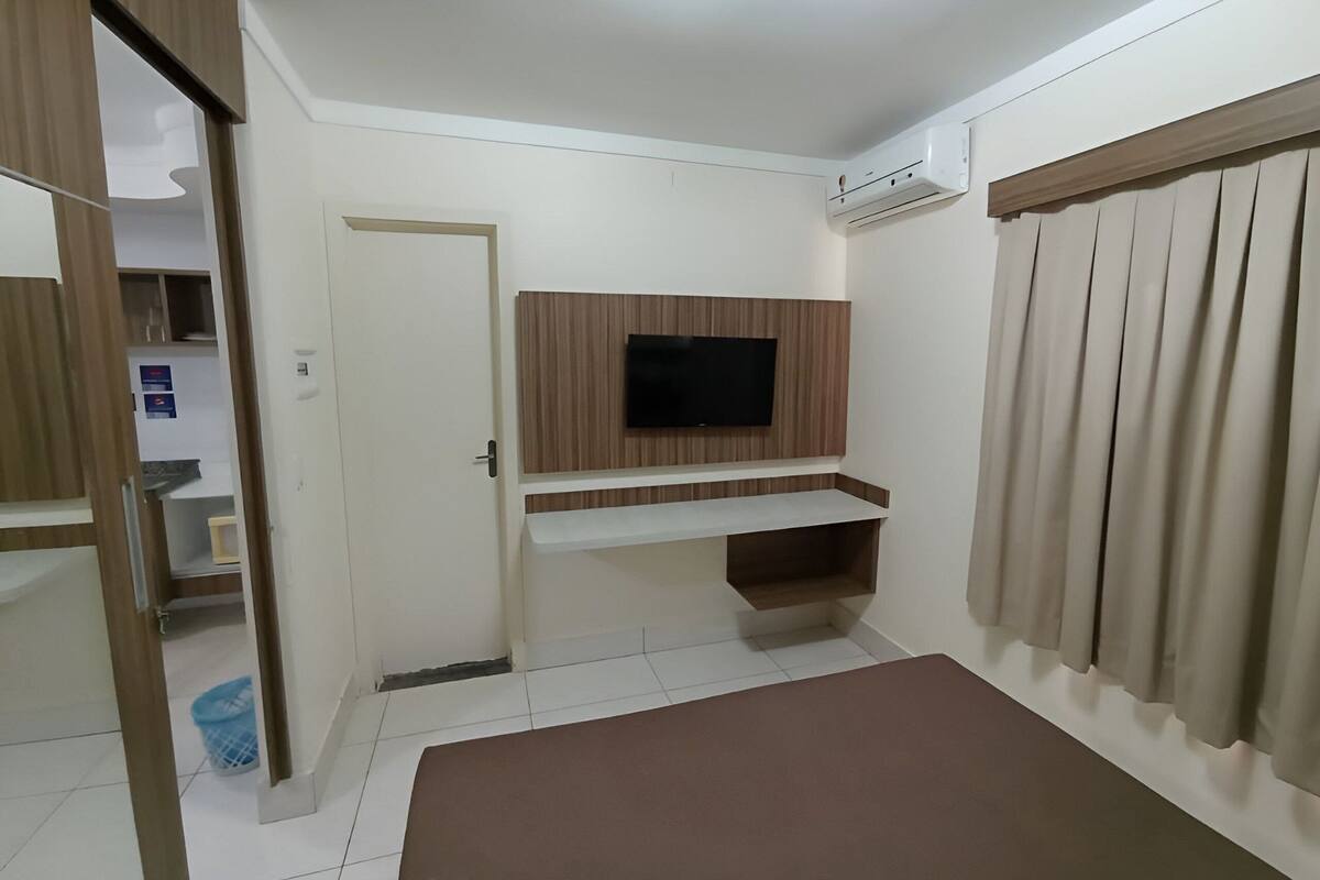 Een slaapkamer met een aan de muur bevestigde televisie, een bed, een deur en een raam met gordijnen.