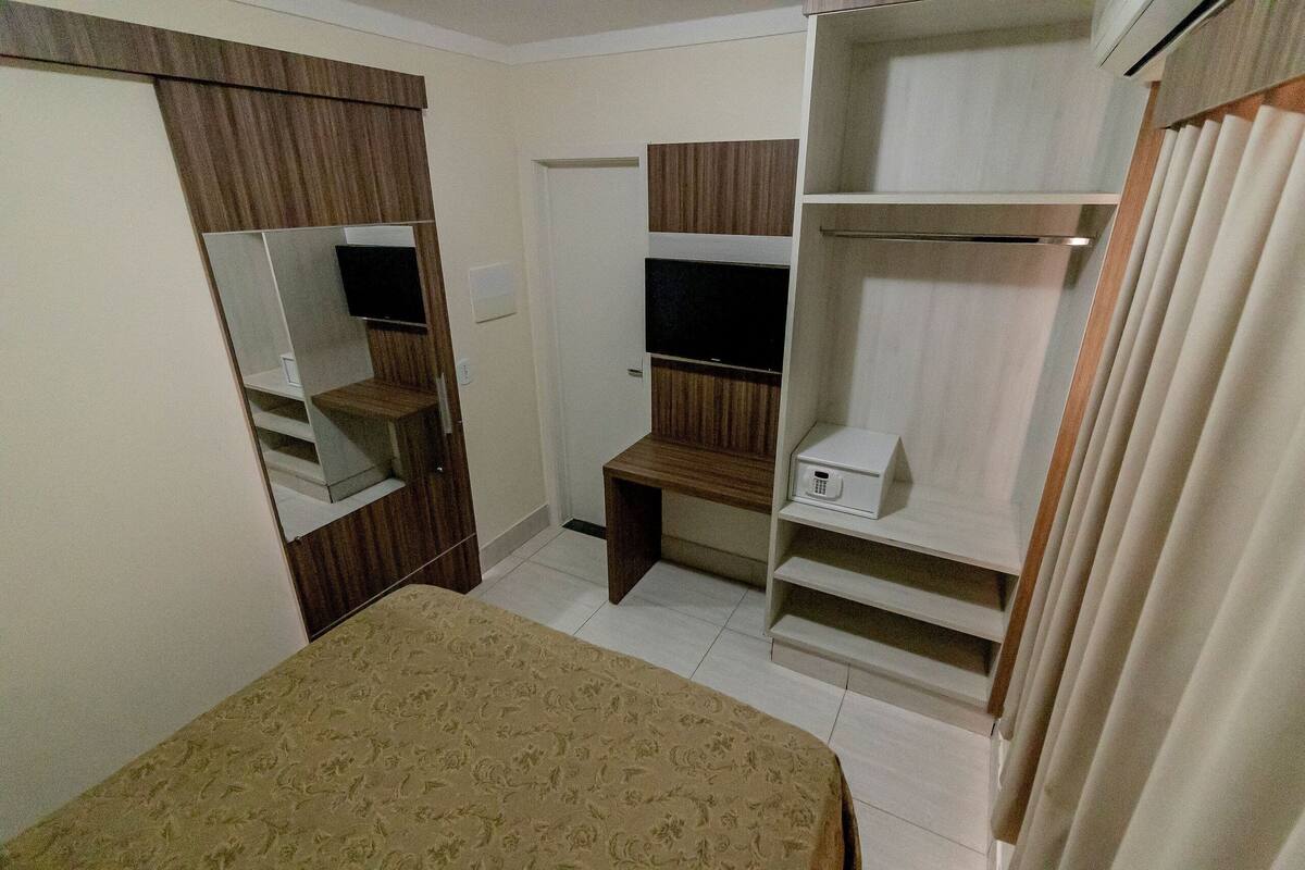 Een slaapkamer met een bed, een garderobe met spiegels, een bureau en planken.