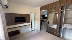 A bedroom with a bed, a TV mounted on a wall, a wardrobe, and a small kitchenette area.