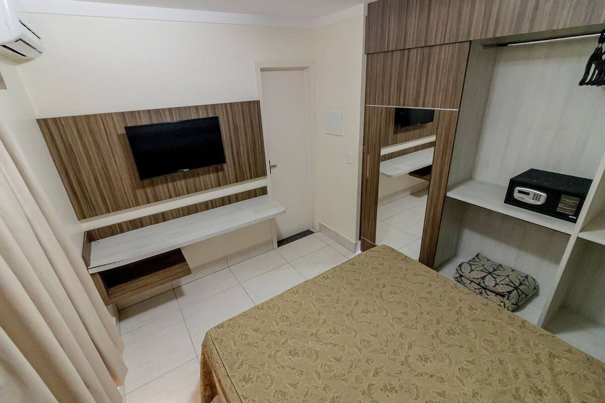 Een slaapkamer met een bed, een aan de muur bevestigde televisie, een kledingkast en een nachtkastje.