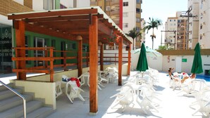 A rooftop pool area with white lounge chairs and a wooden pergola.