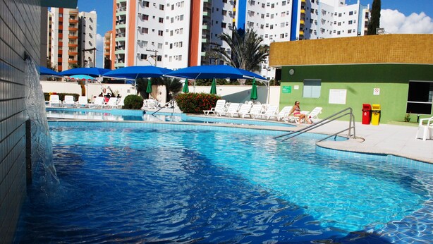 A swimming pool with lounge chairs and umbrellas, surrounded by high-rise buildings.