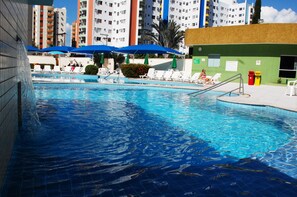 Ein Schwimmbecken mit Liegestühlen und Sonnenschirmen, umgeben von Hochhäusern.