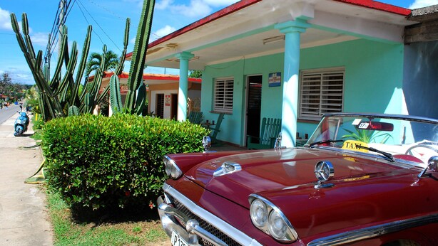 Un coche rojo antiguo estacionado frente a un edificio turquesa con techo rojo.