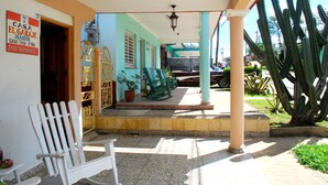 Un espacio al aire libre cubierto con una silla blanca, un letrero que dice 'Casa El Garage' y un cactus grande al fondo.