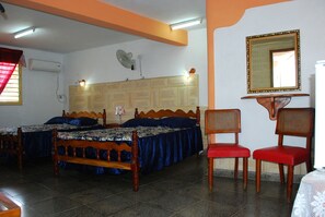 A room with two wooden beds, a red chair, a table, and a mirror on the wall.
