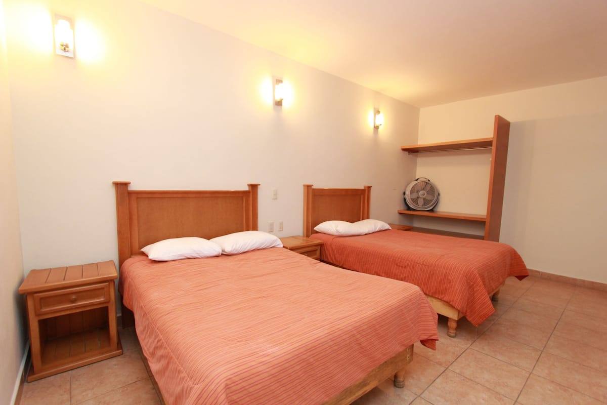 Hotellihuone, jossa on kaksi erillistä sänkyä, puiset päätyosat ja pieni yöpöytä, jossa on lamppu.