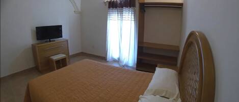 A bedroom with a bed, a TV on a wooden cabinet, a window with curtains, and a staircase.
