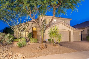A two-story house with a garage, surrounded by a landscaped garden with various plants and a tree.