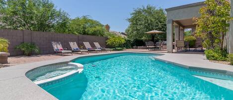 A swimming pool with a curved edge, surrounded by lounge chairs and a patio area with outdoor furniture.