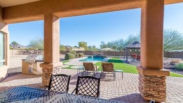 A covered patio with a pool, outdoor seating, and a view of the backyard.