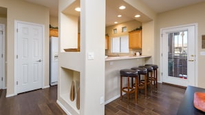 A modern kitchen with a central island, wooden bar stools, and a sliding glass door leading to a patio. - Raintree 2 Bedroom Condo by RedAwning (Scottsdale)